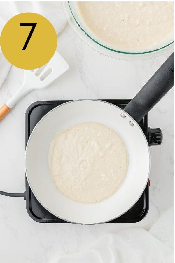 A ladle of lemon ricotta pancake batter cooking in an oiled pan.