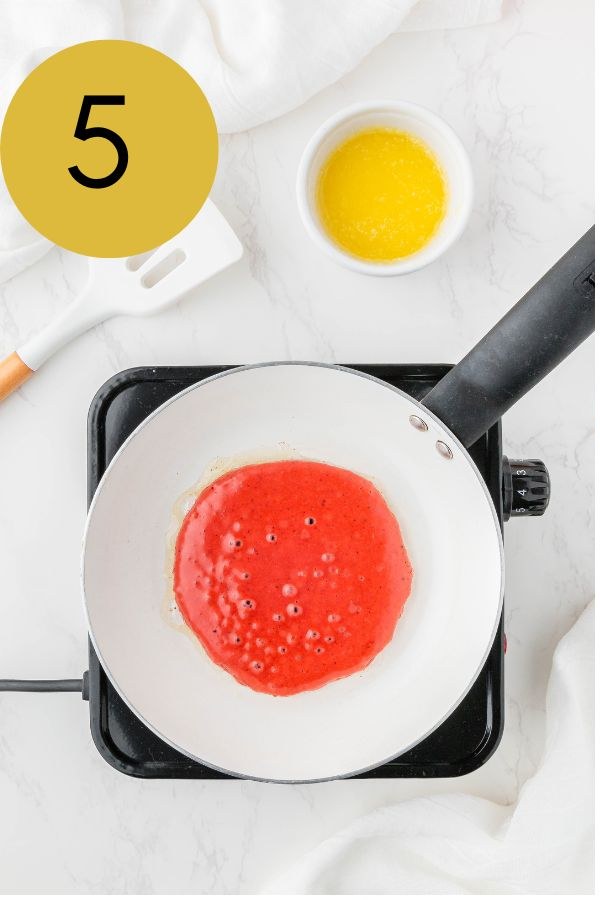 Red velvet pancake batter bubbling in a buttered skillet.
