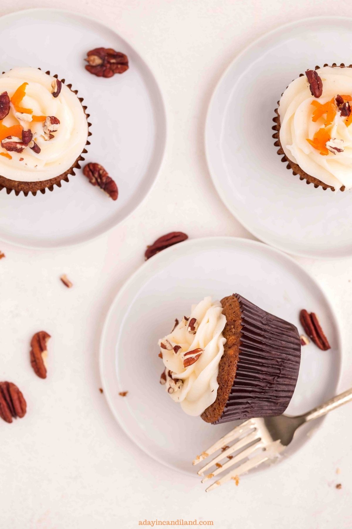 3 carrot cake cupcakes on three plates with a gold fork.