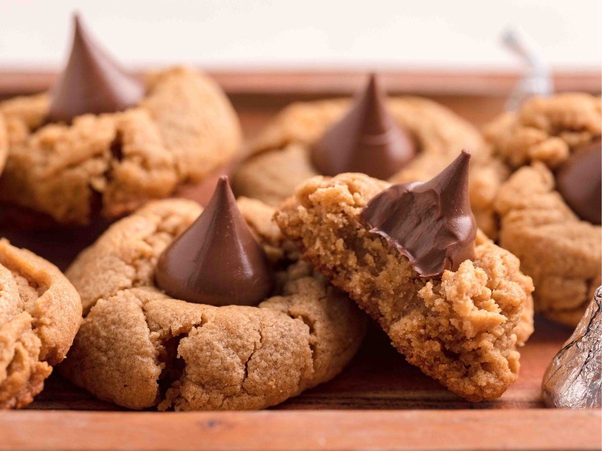 Wood board with Peanut Butter Cookies with Hersheys Kisses. One cookie with a bite out of it.