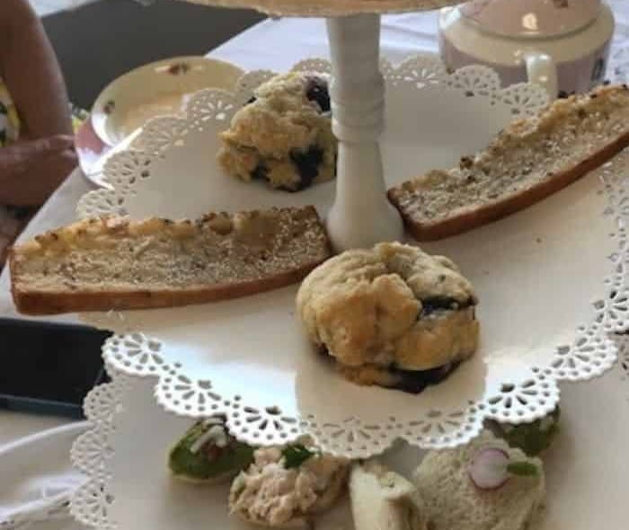 A three tiered tea tray with scones, tea bread and tea sandwiches.