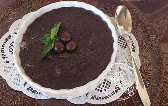 Mocha creme brulee garnished with mint and espresso beans on a lace doily with a spoon.