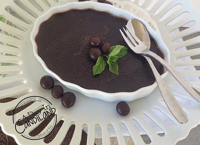 A mocha espresso creme brulee in a white fluted ramekin with chocolate covered espresso beans, fresh mint and a spoon.