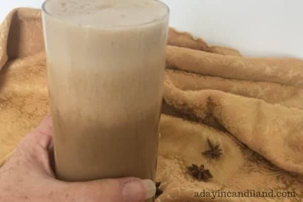 Hand holding glass of chai tea smoothie on a gold tablecloth