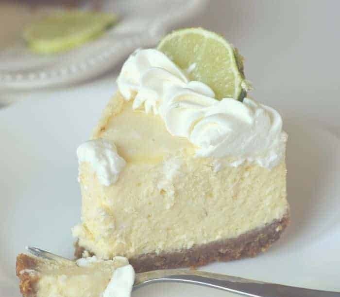 A slice of key lime cheesecake with whipped cream and a lime slice on a white plate.