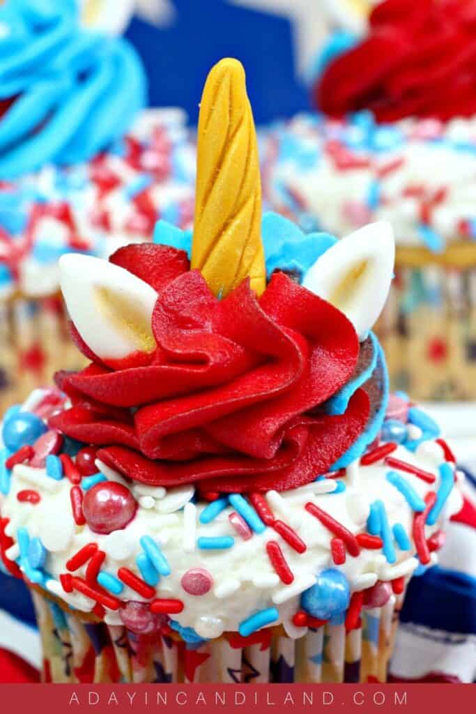 table with red white and blue frosted cupcakes with unicorn ears and horn.