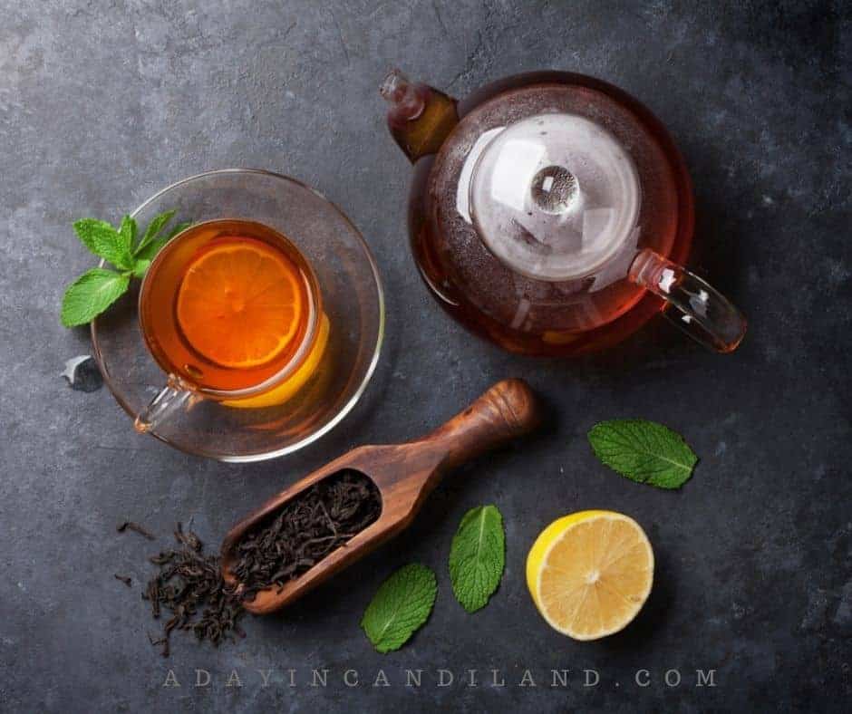 A clear teapot full of tea with a teacup and lemon on a table. 