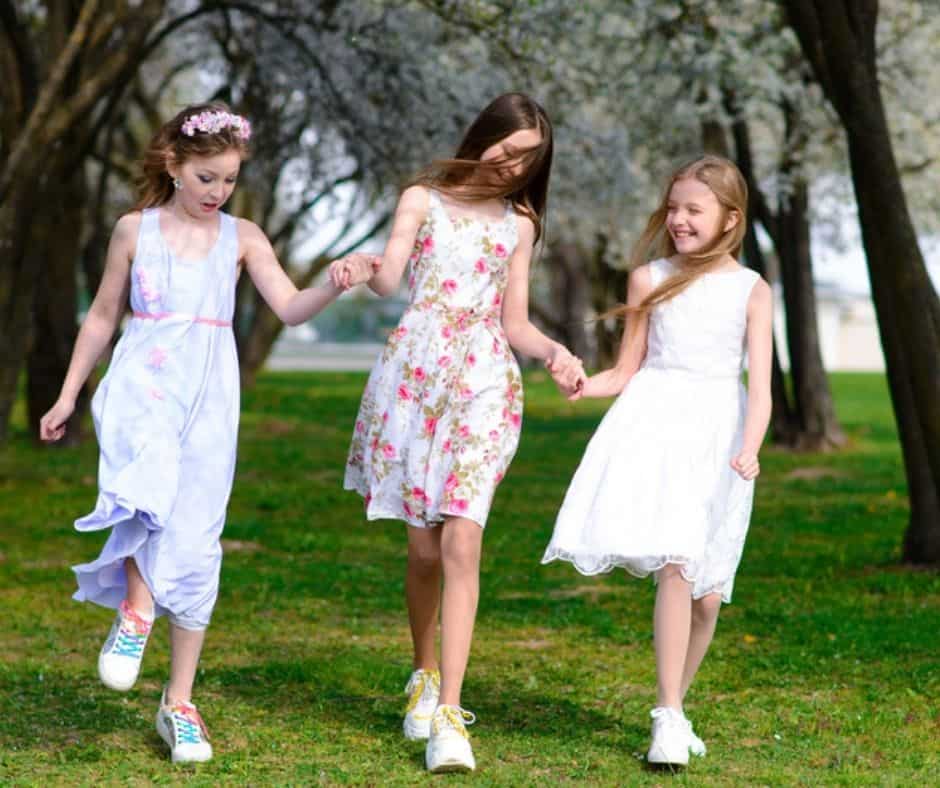 3 girls dress up for tea holding hands in the park 