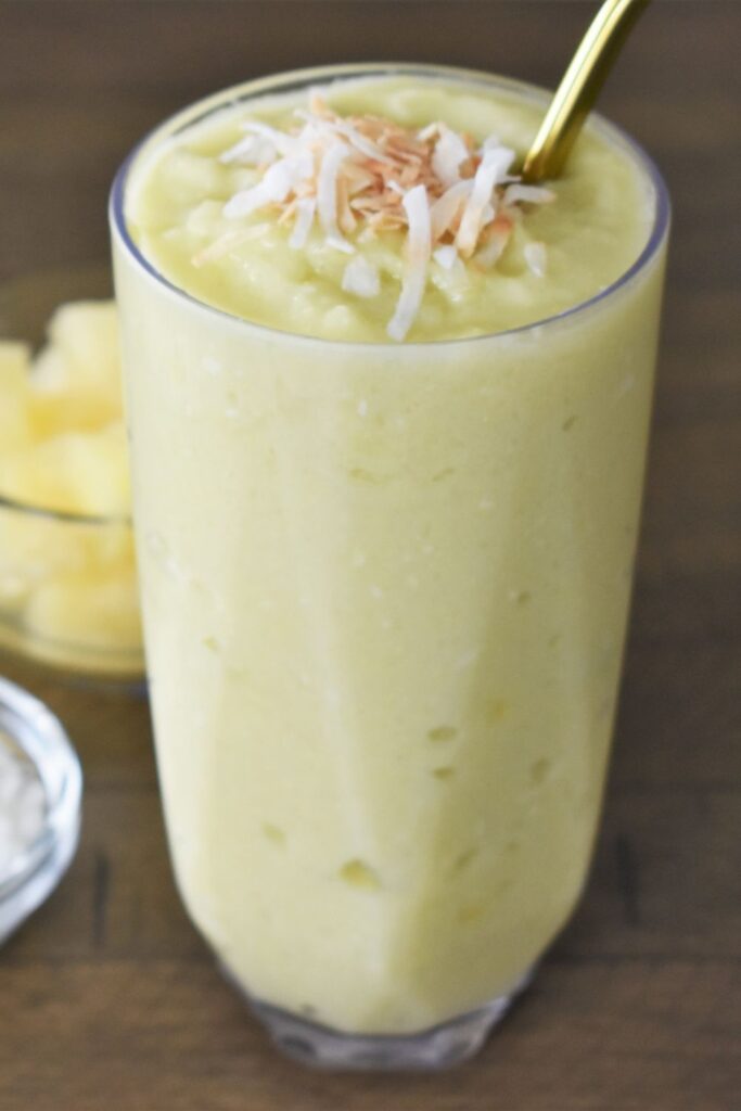 Glass of Pineapple Avocado Smoothie with gold metal straw and toasted coconut. 