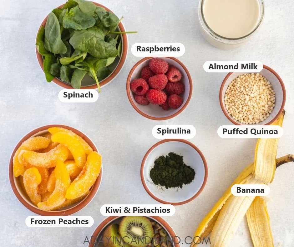 Labeled green smoothie bowl ingredients: spinach, raspberries, almond milk, puffed quinoa, spirulina, frozen peaches, banana, kiwi and pistachios.