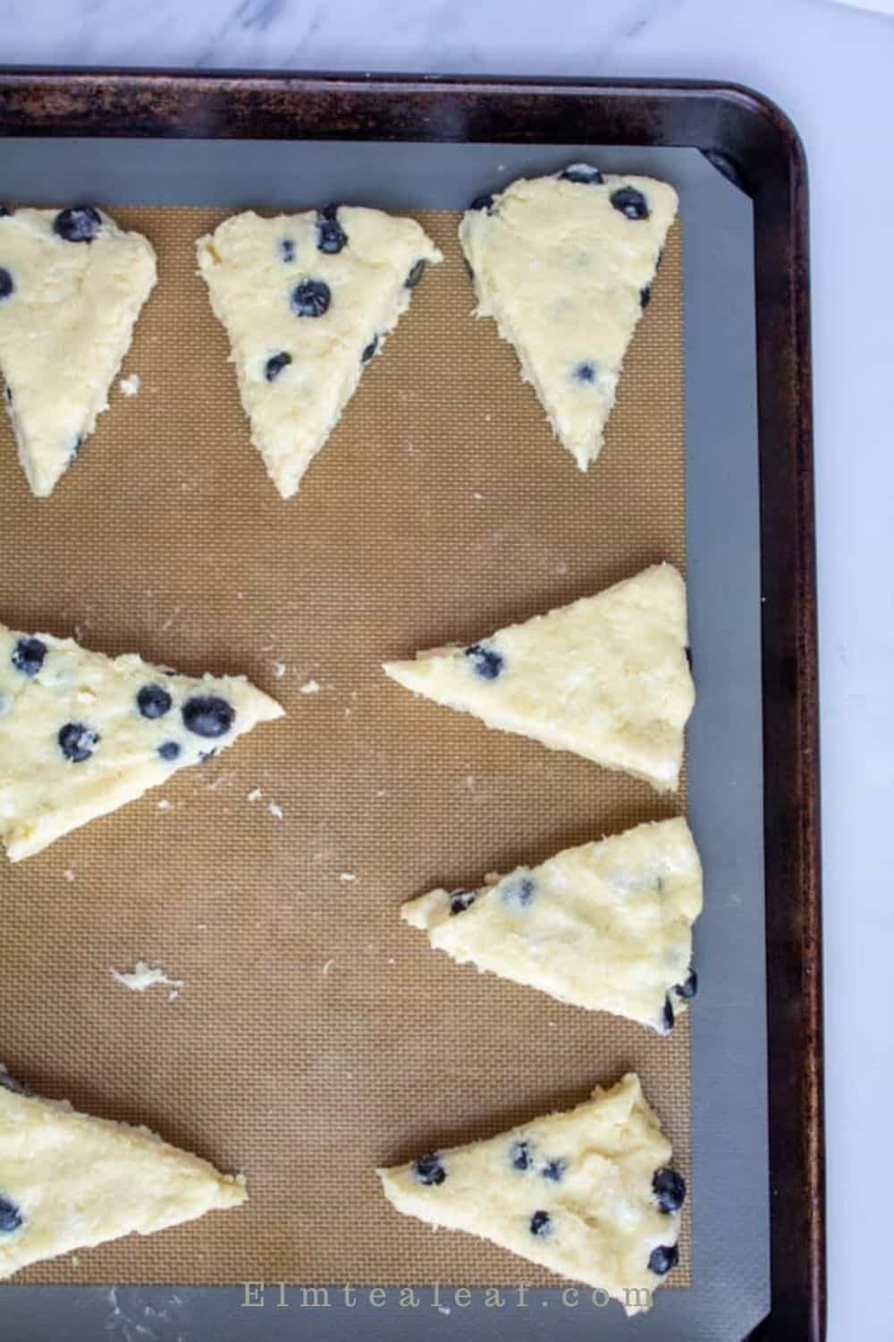 Blueberry scone wedges separated on a parchment lined baking sheet, sprinkled with cinnamon sugar.