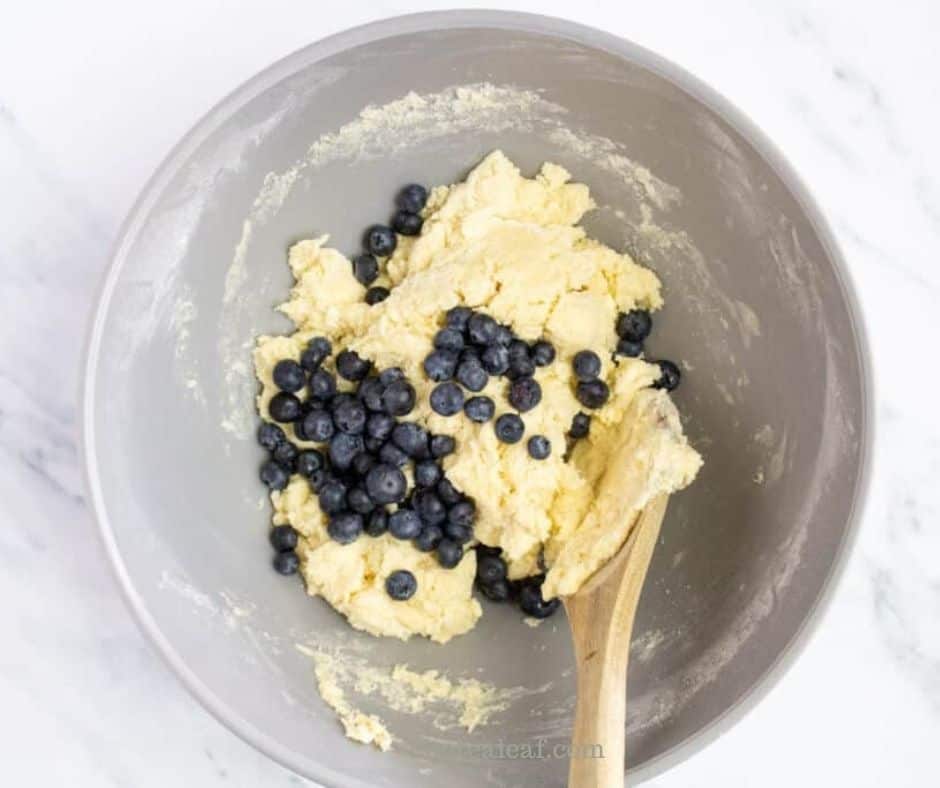 Fresh blueberries folded into the soft scone dough with a wooden spoon.