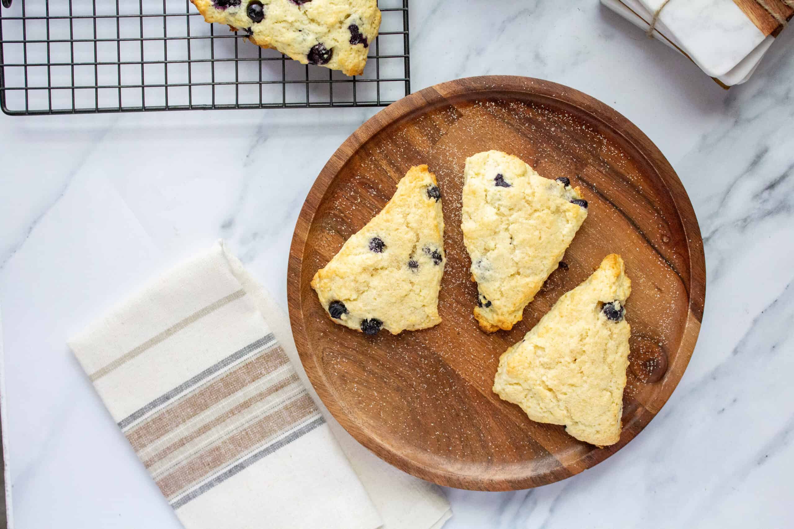 Three blueberry scones on a wooden plate beside a white napkin.