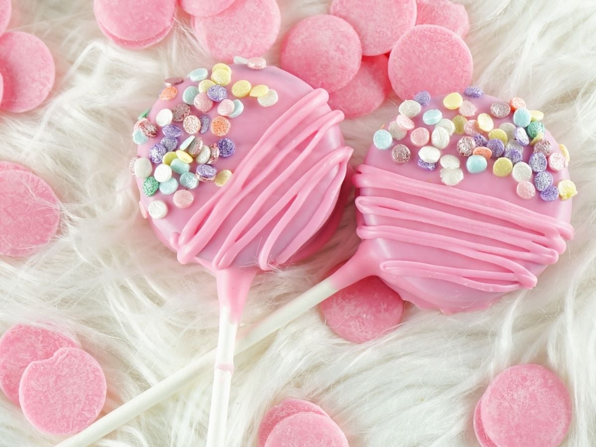 Two finished Oreo pops lying on white fur with pink candy melts scattered around.