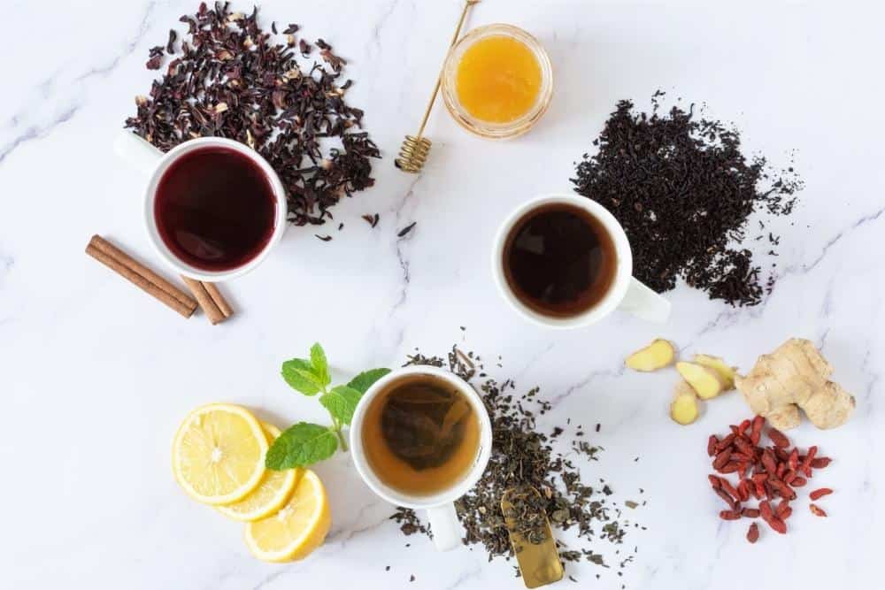 3 Cups of Tea with loose tea on marble counter.