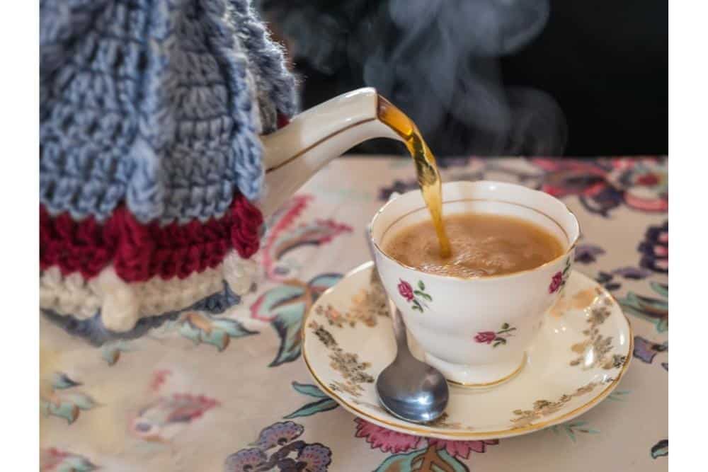 Teapot with tea cozy on pouring cup of tea. 