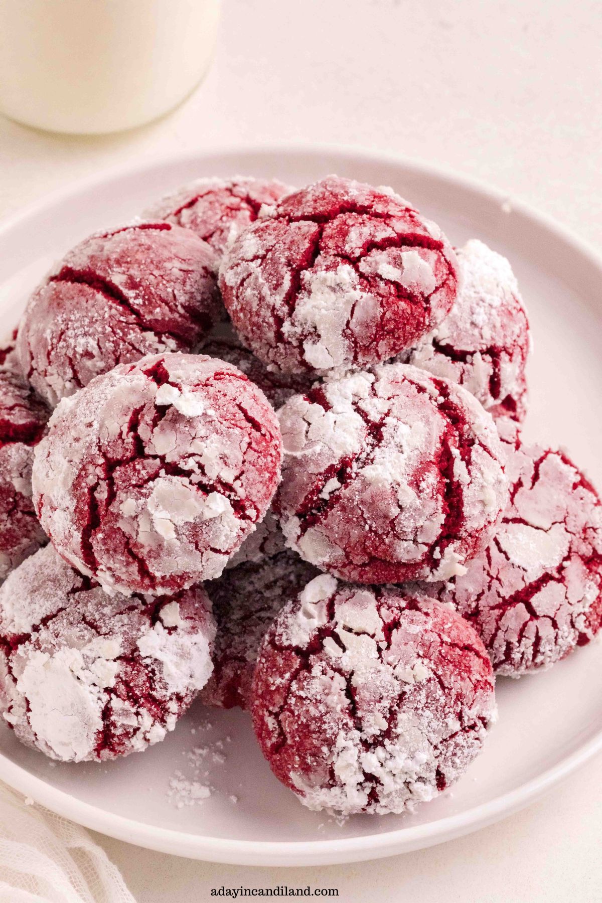 A plate of Red Velvet Cookies stacked with a glass of milk.