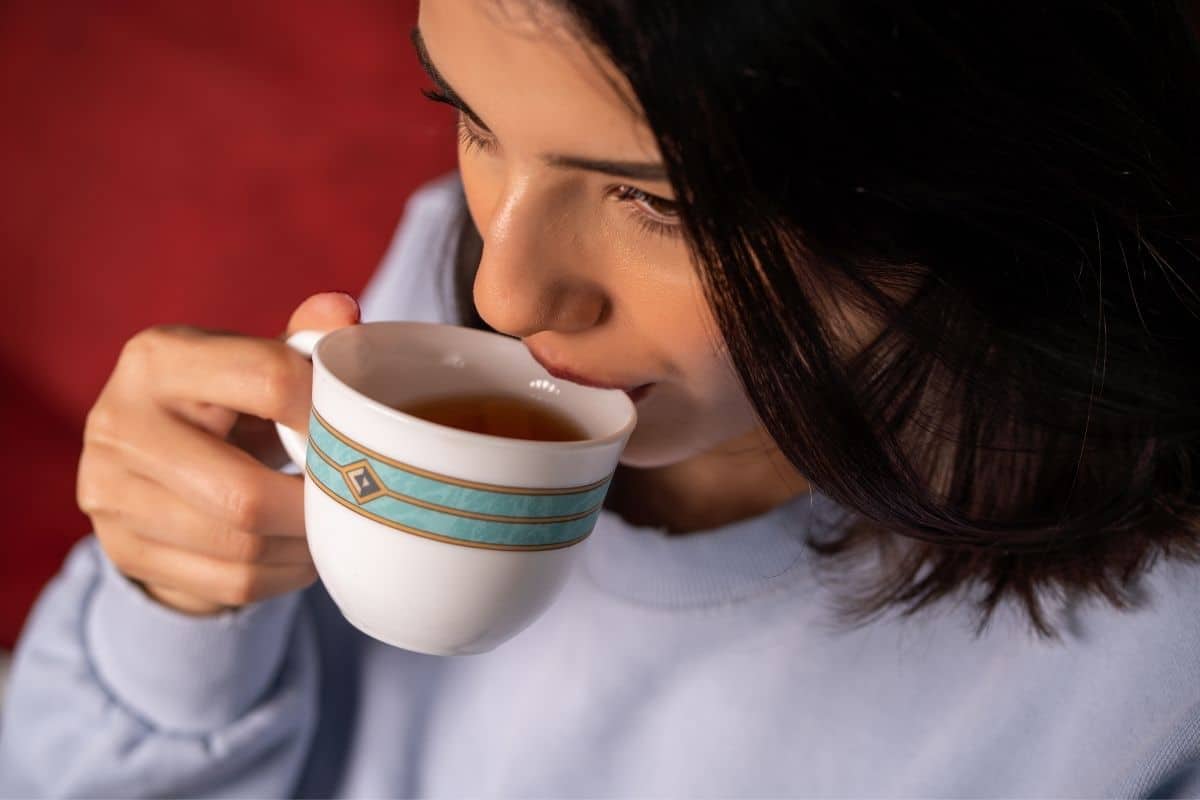 A woman taking a sip of tea from a teacup. 
