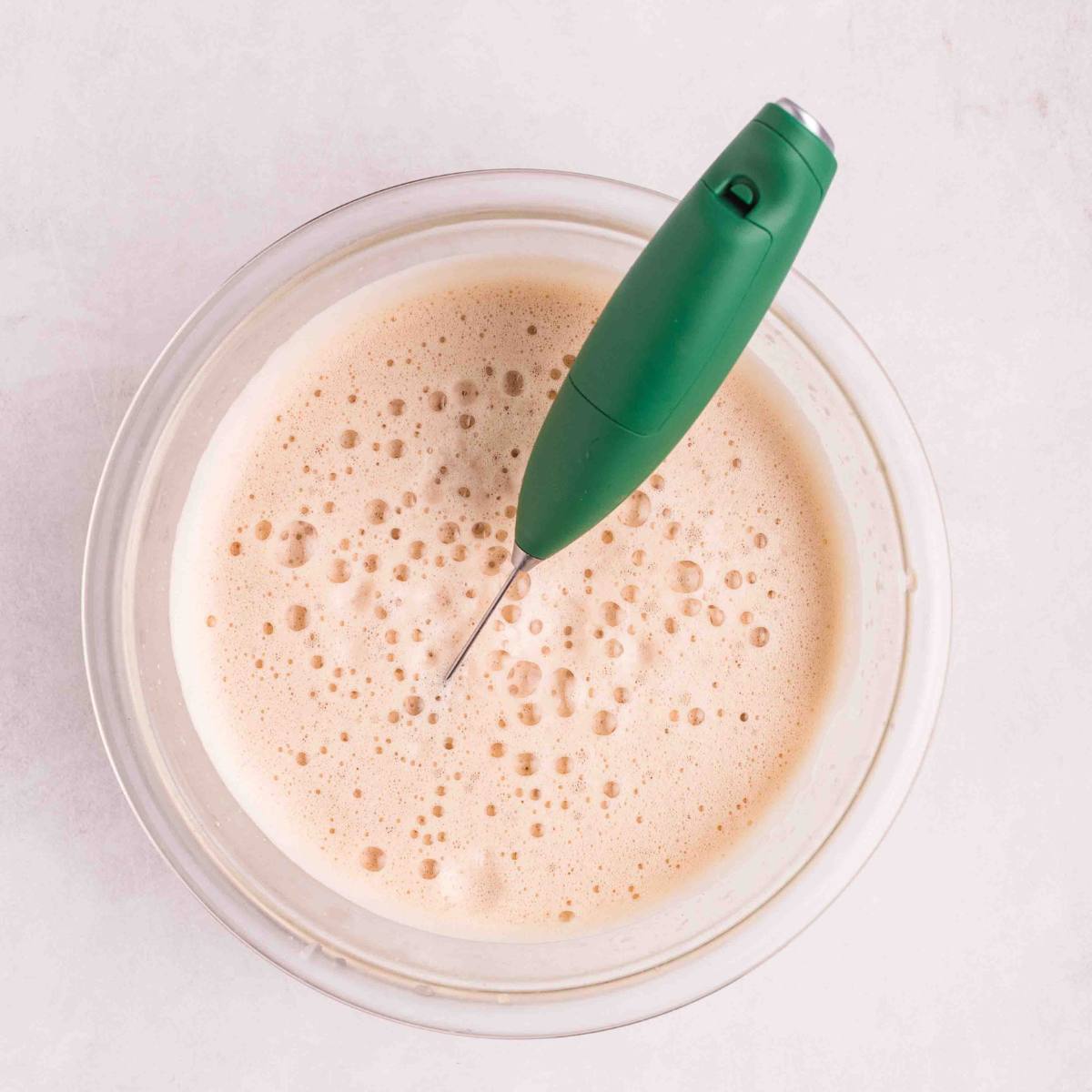 A handheld frother foaming the espresso and milk mixture.