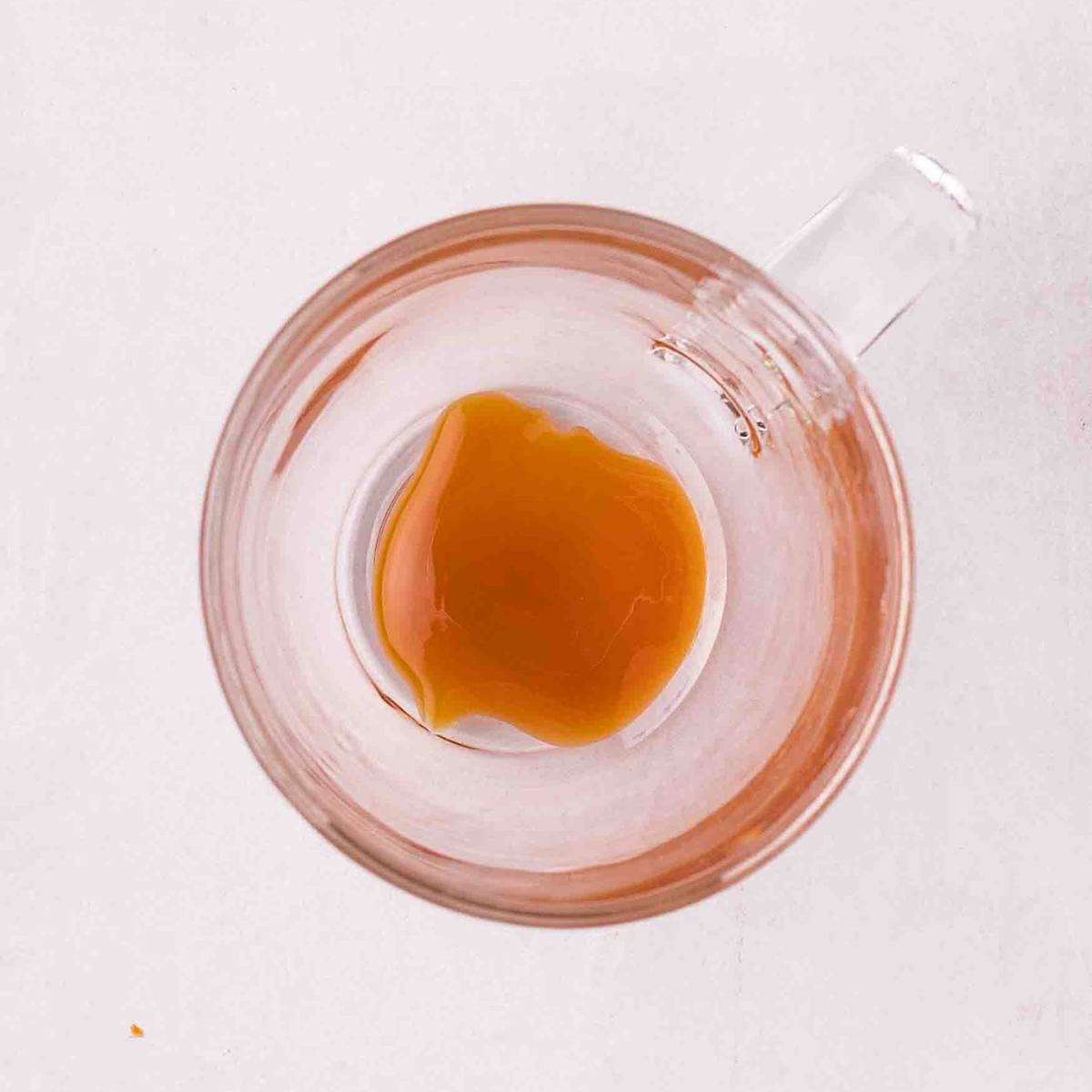 Caramel sauce coating the bottom and sides of a glass mug.