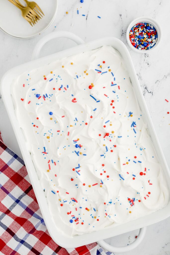 White baking pan of patriotic poke cake with red white, blue and gold sprinkles. 