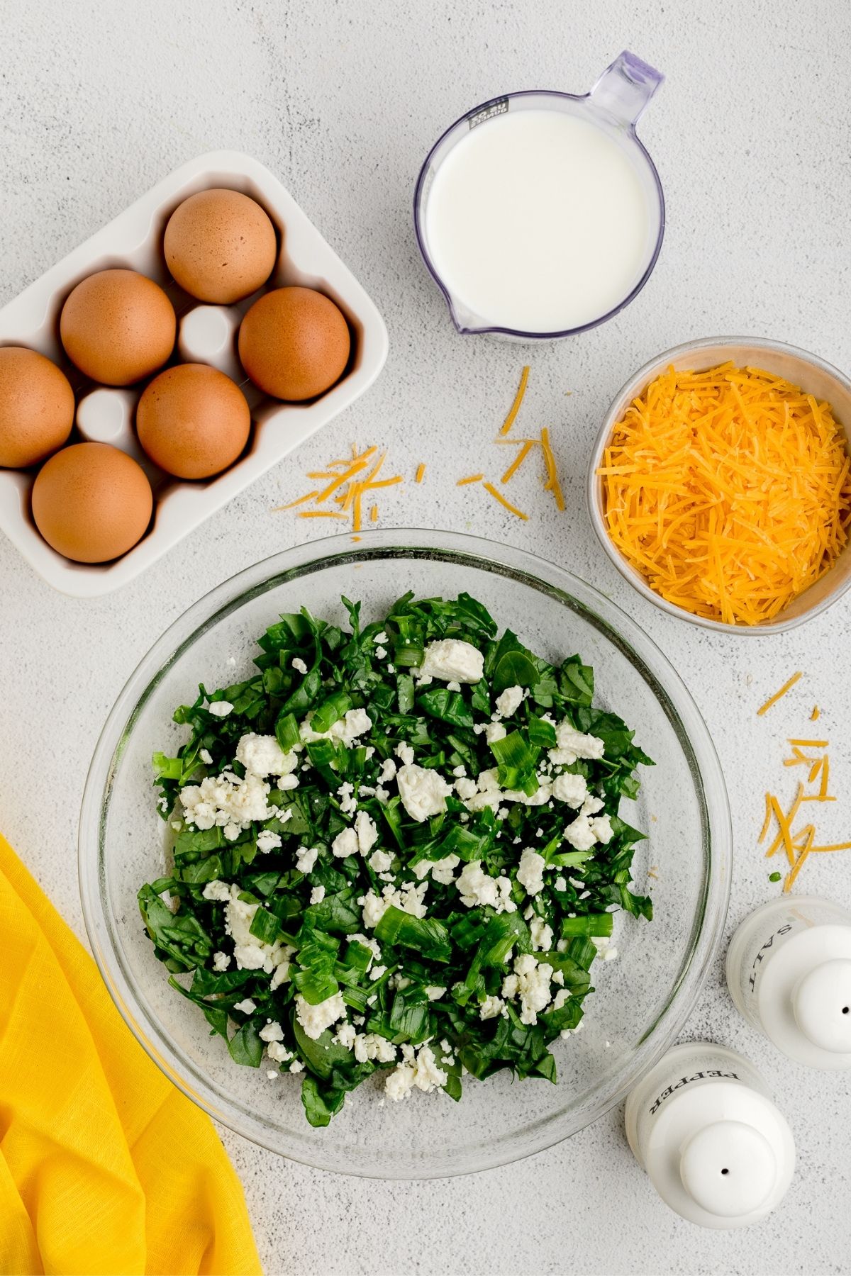 Crumbled feta cheese scattered over the chopped spinach in the bowl.