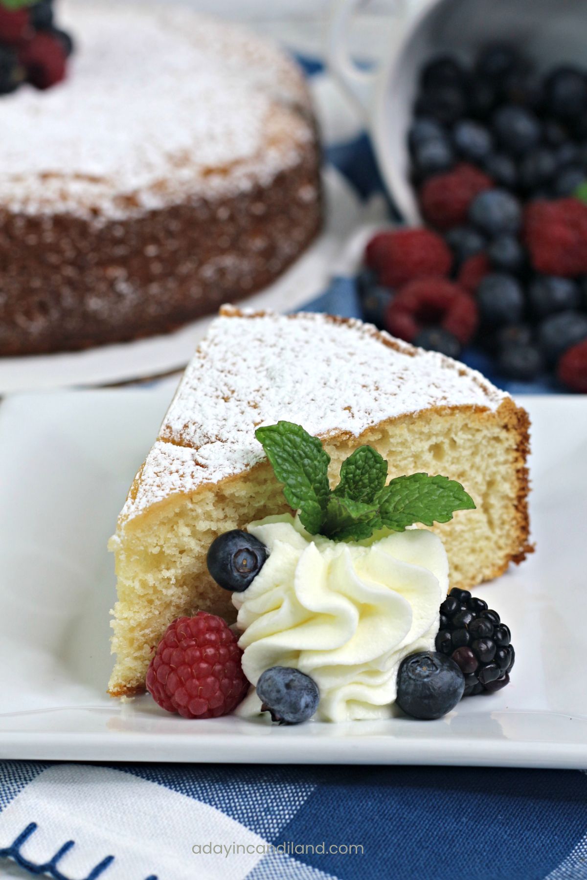 Slice of Tea cake with mint and whipped cream on a plate with a few berries. 