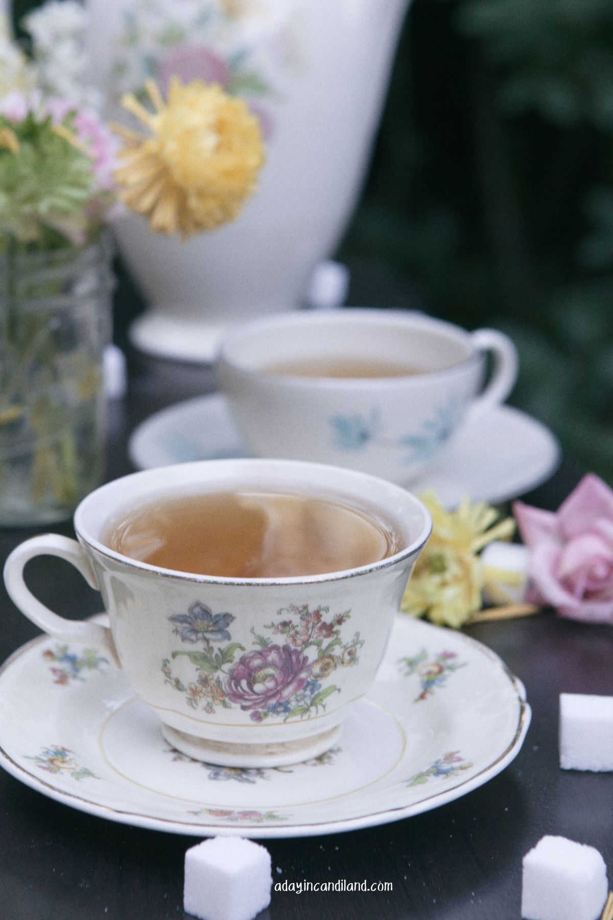 Table with cup of tea, flowers, and teapot. 