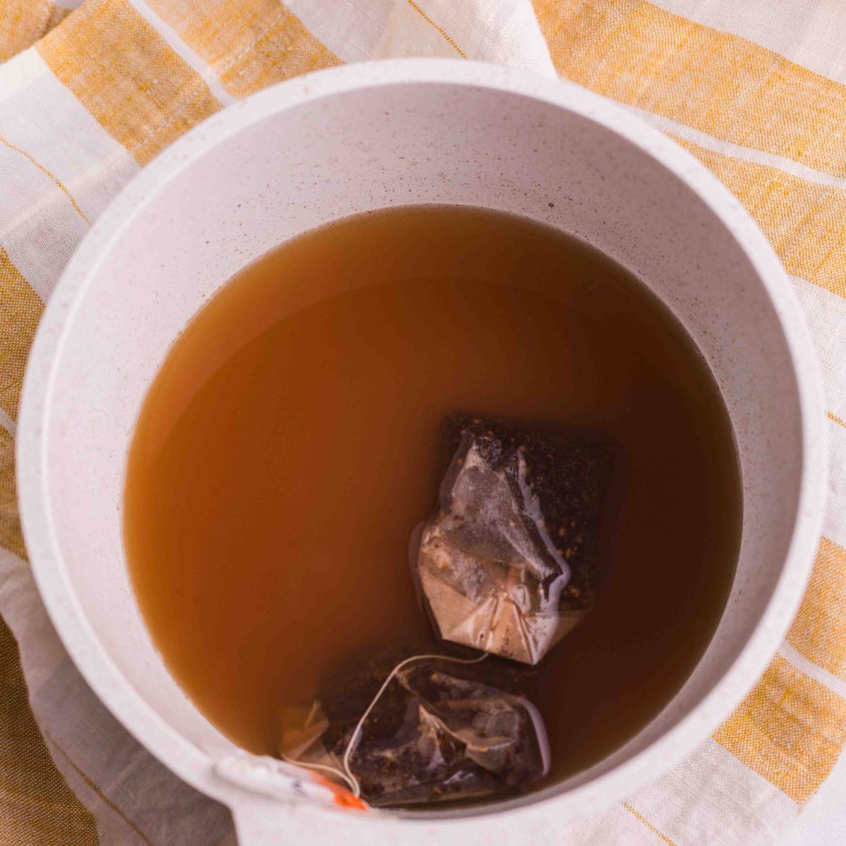 Chai tea bags steeping in water in a white saucepan.