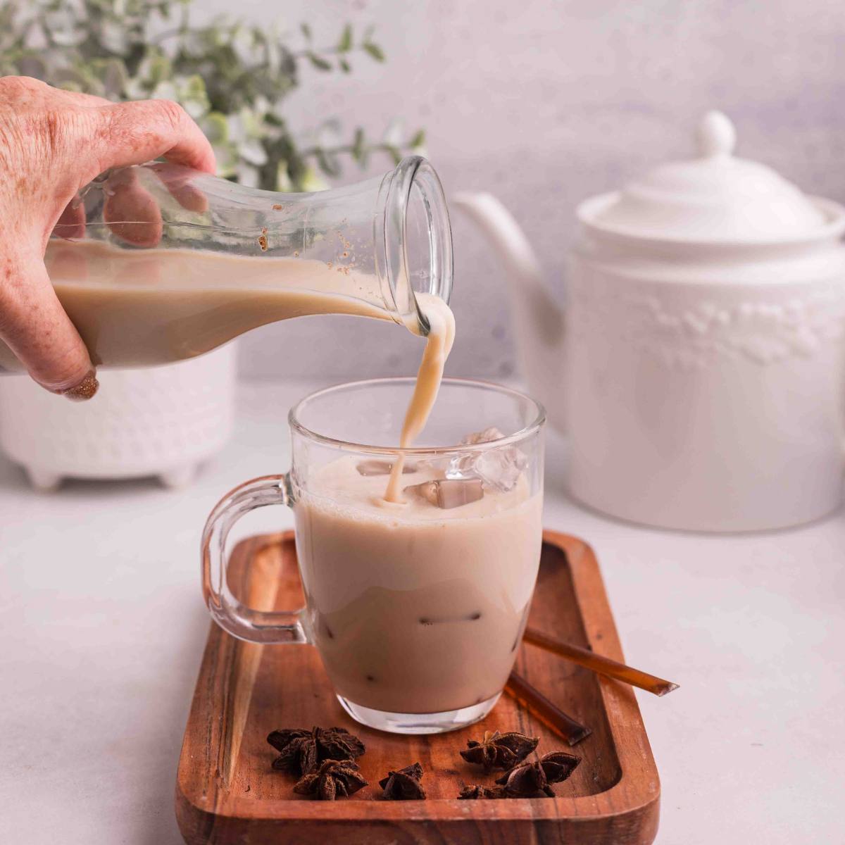 Chai latte being poured over ice into a glass mug.