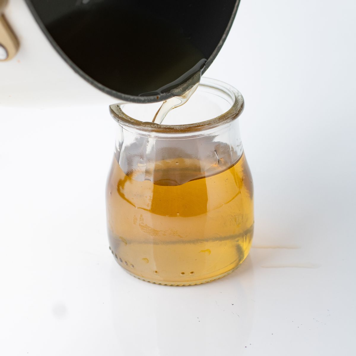 The golden vanilla simple syrup poured from the saucepan into a small glass jar.