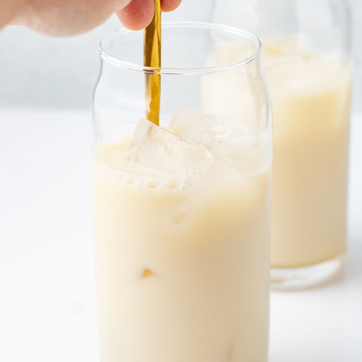 Oat milk over ice in a tall glass, stirred with a gold spoon.