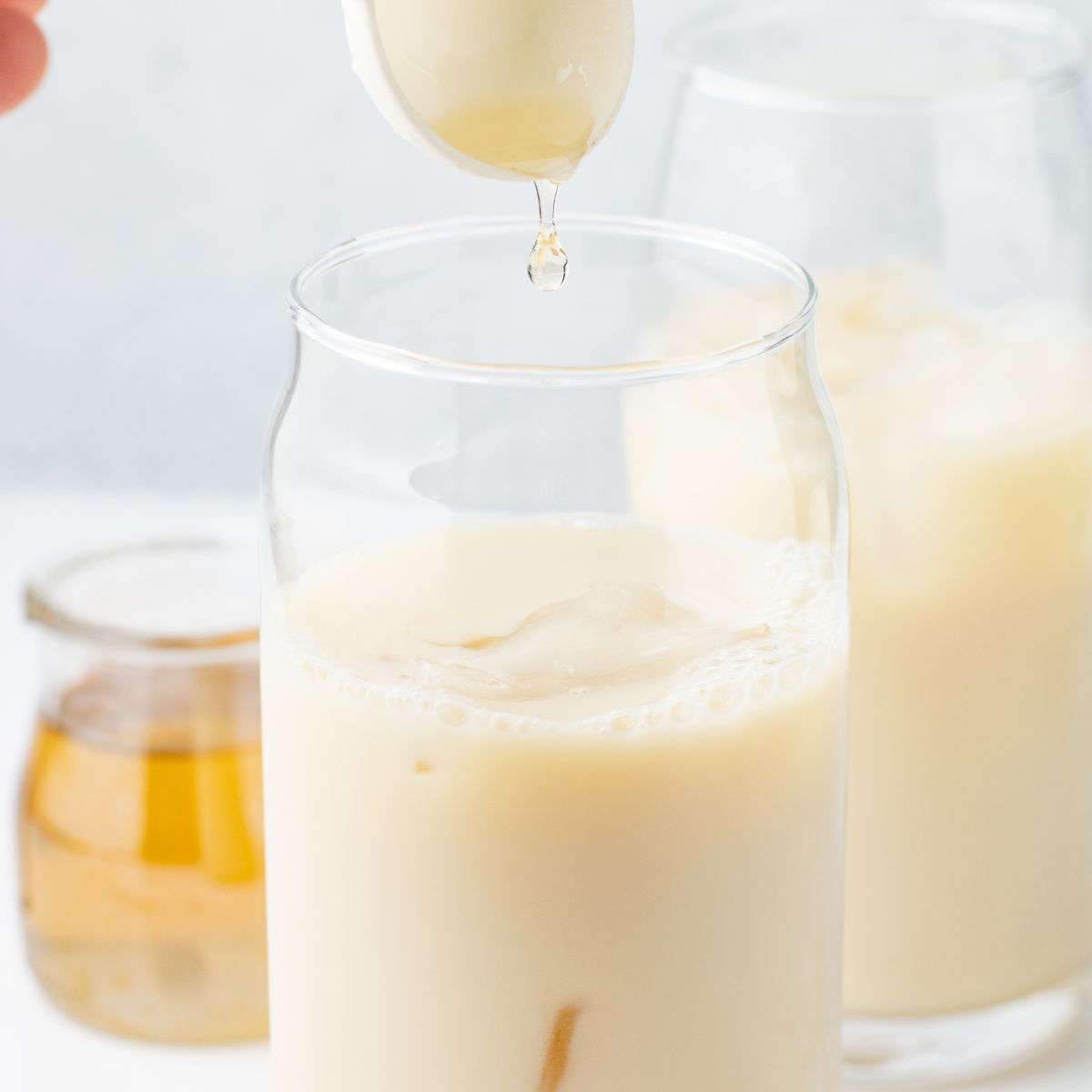 Vanilla simple syrup poured into the glass of iced oat milk.