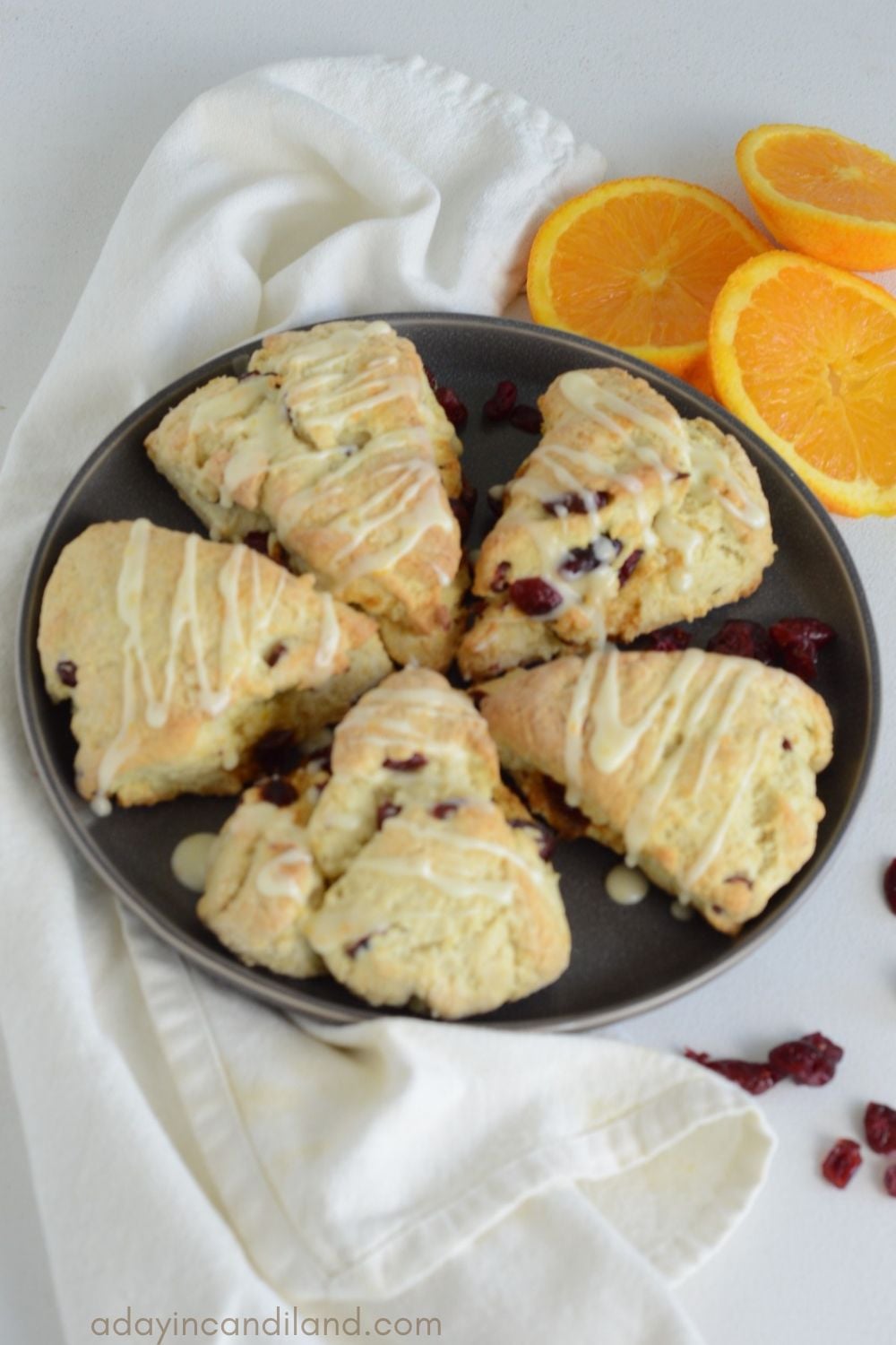 Grey round plate of Cranberry Scones with orange slices and a white napkin.