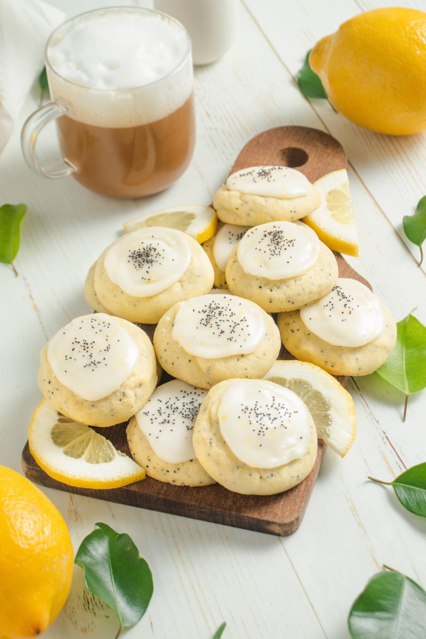 Lemon Poppy Seed Cookies on a cutting board with lemon leaves and cup of Tea Latte.