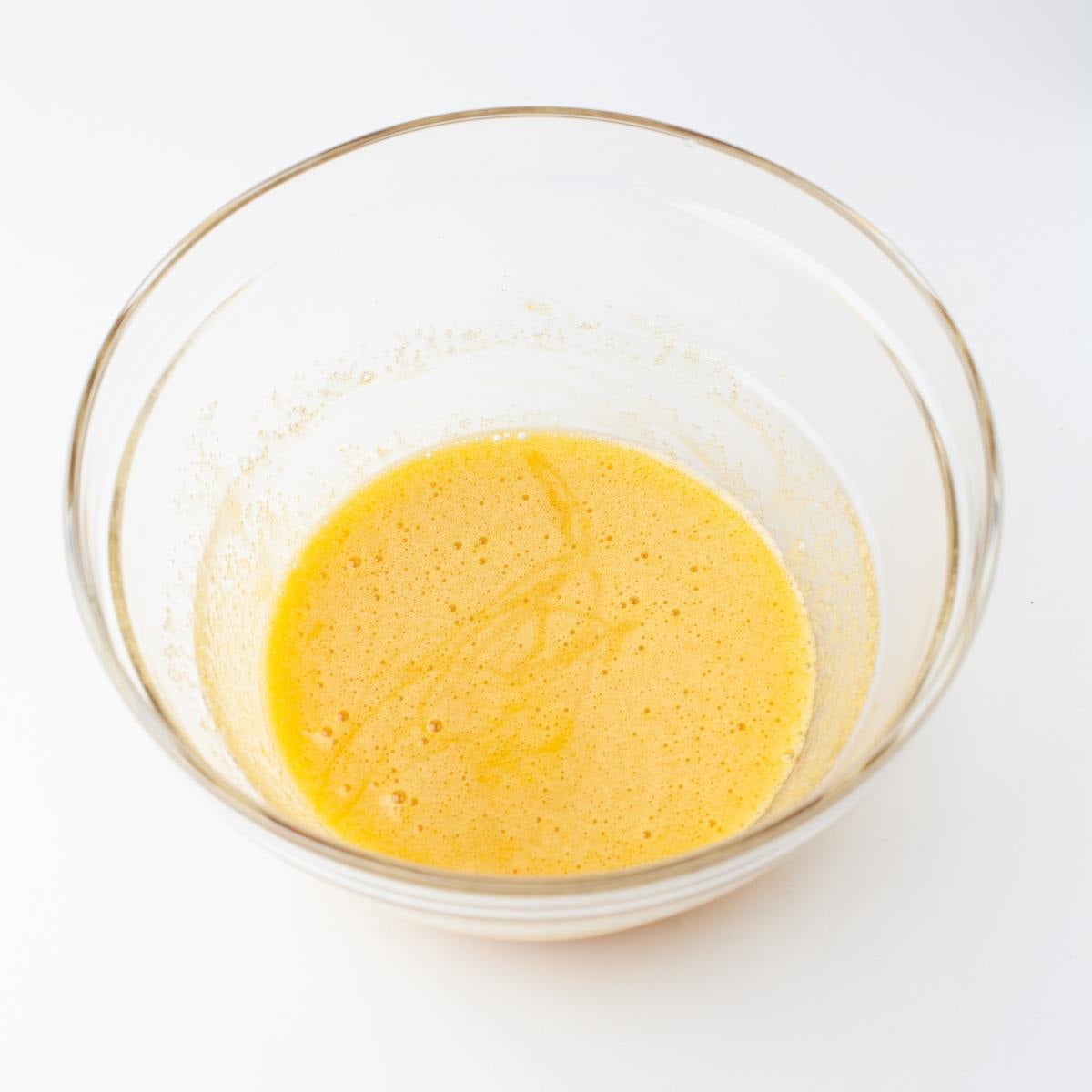 Eggs, sugar and vanilla whisked together in a glass bowl.