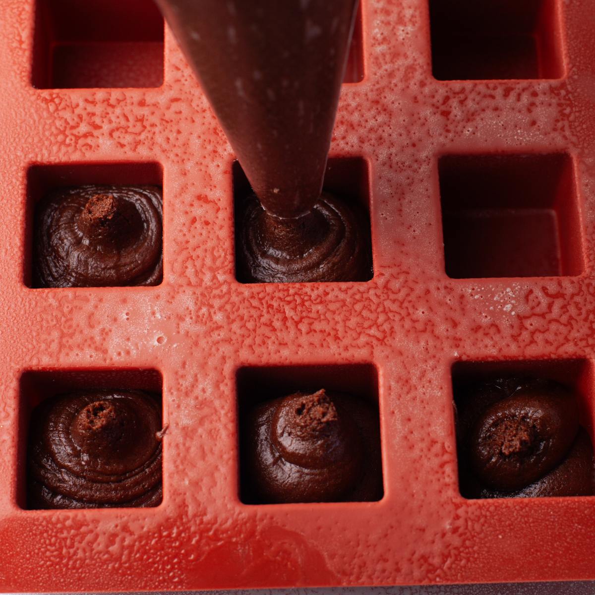 Brownie batter piped into a red silicone square mold.