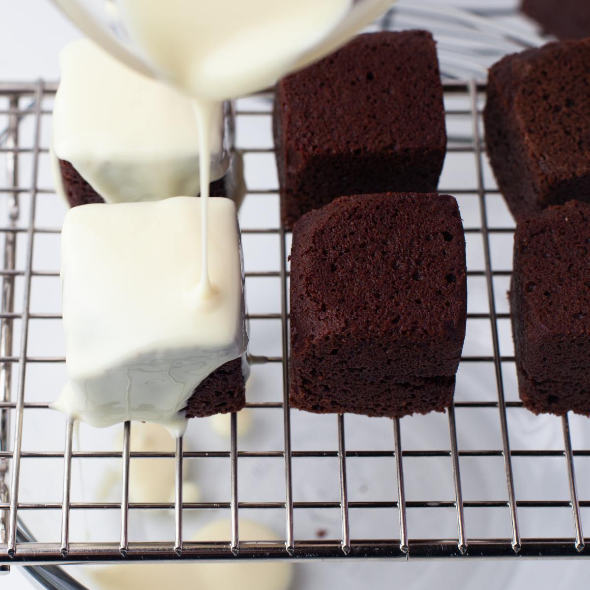 Melted white chocolate poured over baked brownie bites on a wire rack.