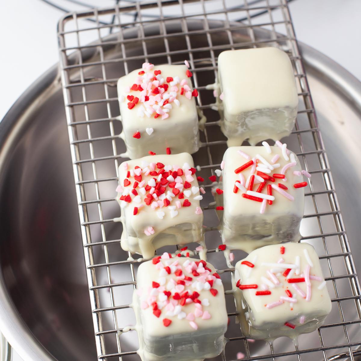 White chocolate coated brownie bites topped with Valentine's sprinkles on a cooling rack.