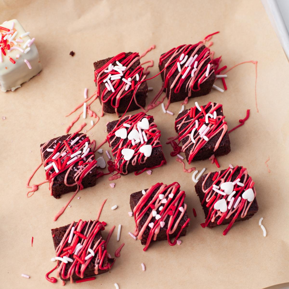 Brownie bites drizzled with red and pink chocolate on parchment paper.