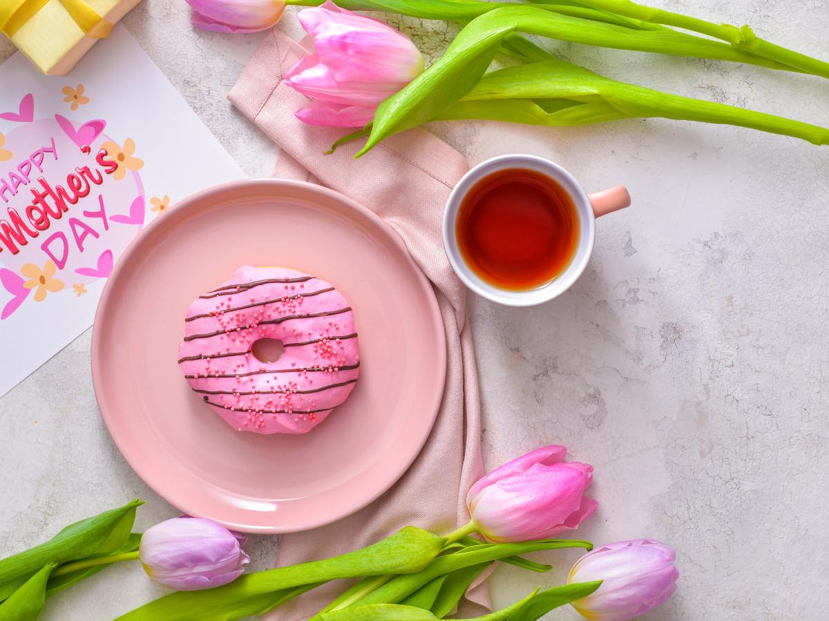 A pink plate with donut, a cup of tea and a Mother's Day Card. 