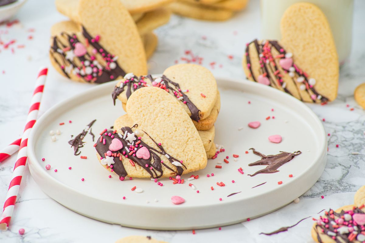 Stacks of Heart Shaped Valentine Sugar Cookie with a chocolate drizzle on top and sprinkles on a white plate.