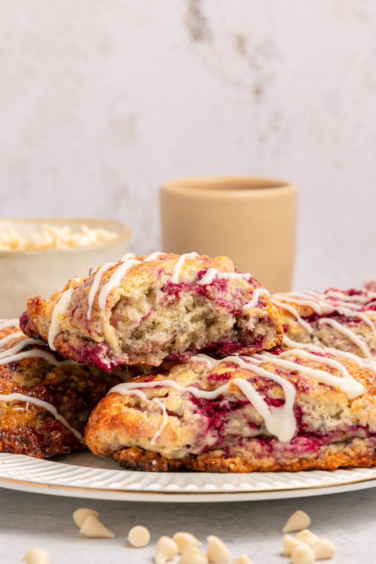 White plate of White Chocolate Raspberry Scones with white chocolate drizzle on top.