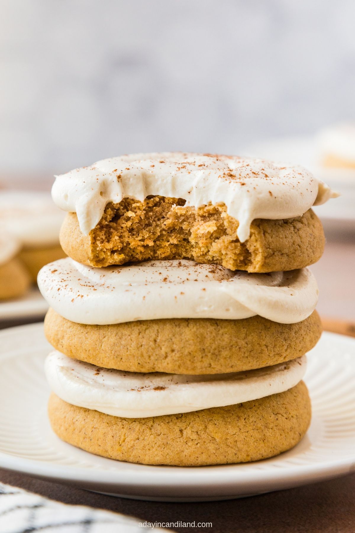 A stack of caramel pumpkin cookies with whipped caramel cream cheese frosting, the top one with a bite taken out.