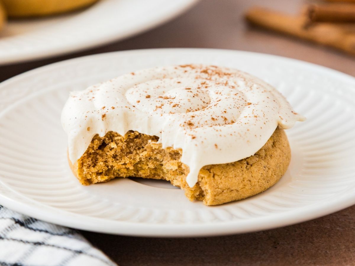 A caramel pumpkin cookie on a plate with a bite taken out, showing the soft center under the frosting.