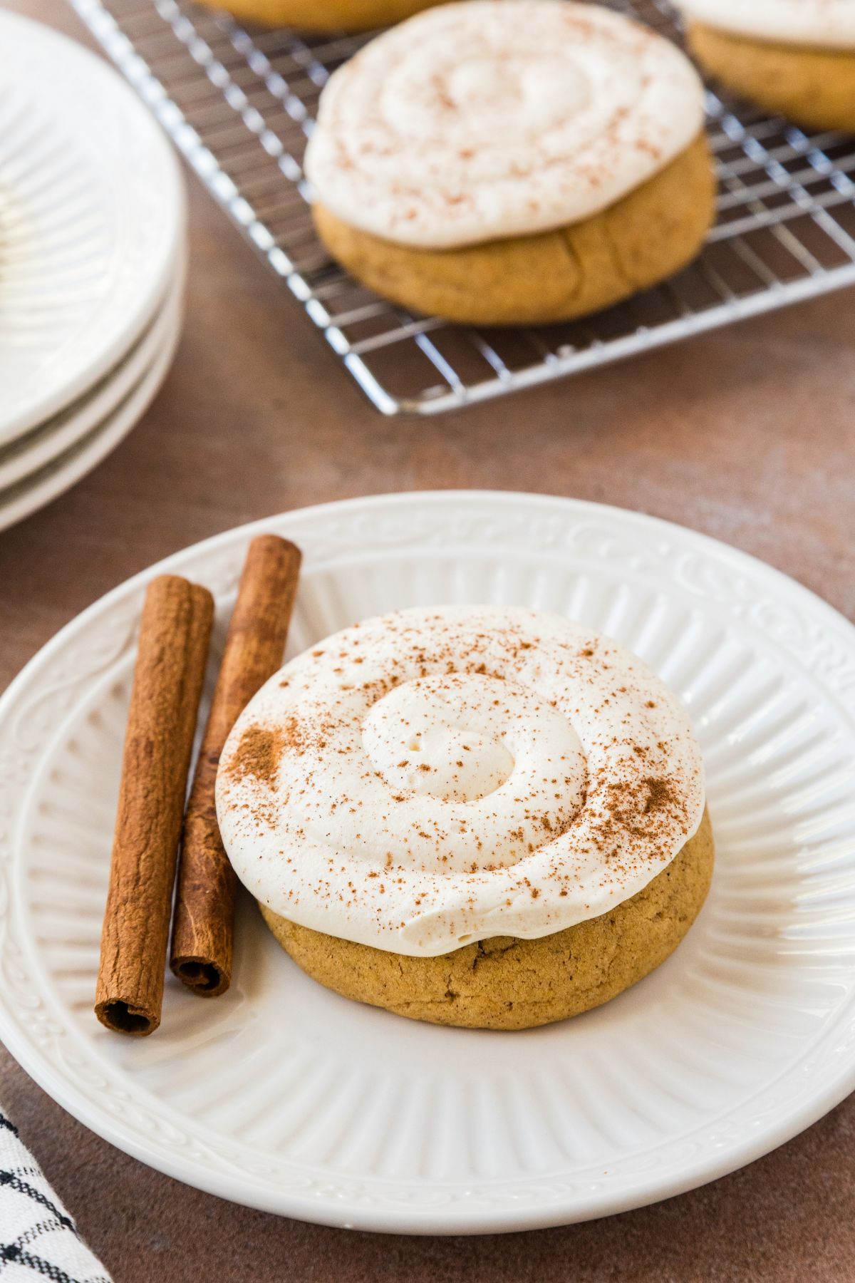 A frosted caramel pumpkin cookie on a white plate beside cinnamon sticks.