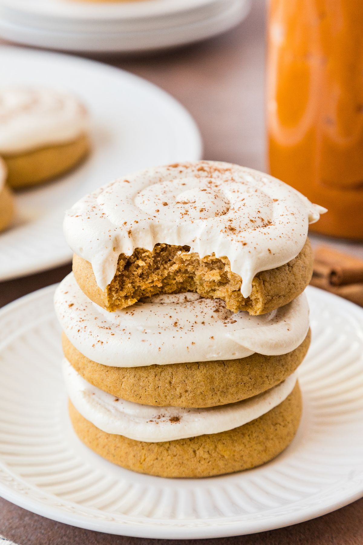 Stacked copycat Crumbl caramel pumpkin cookies on a plate with a jar of caramel sauce behind.