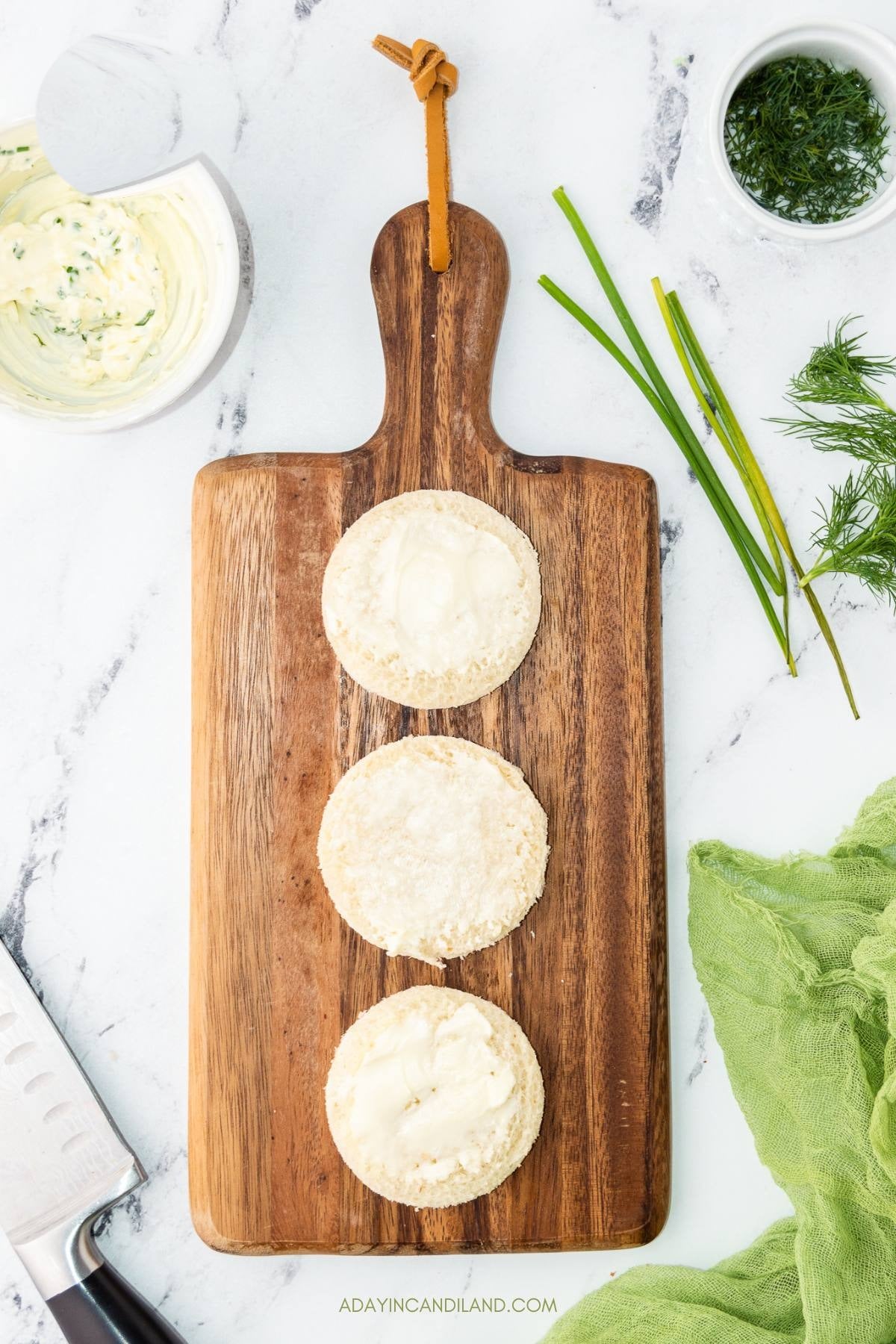 Bread rounds spread with softened butter on a wooden board.