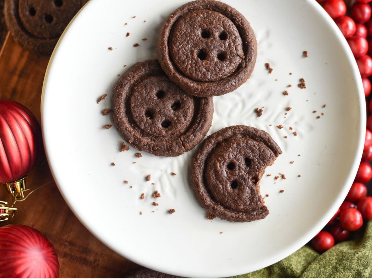 White plate with 3 chocolate button cookies and o bite out of one cookie.