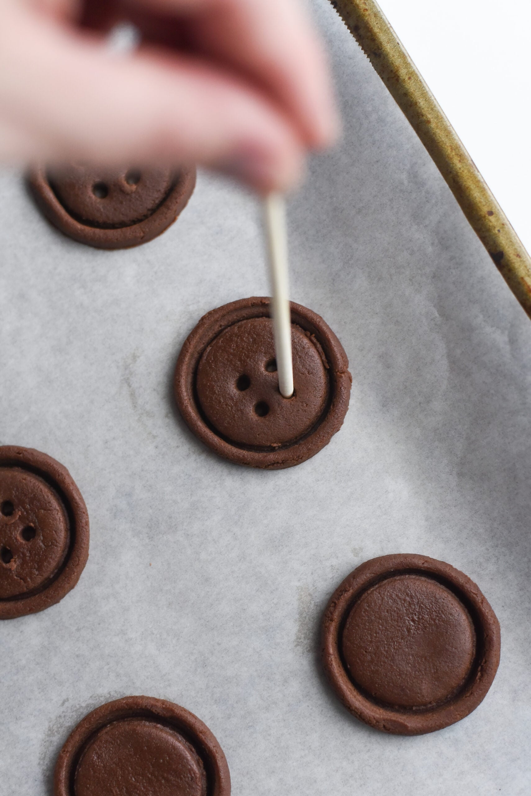 Cookies rolled out on parchment with skewer making button holes.